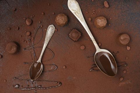 Chocolate covered spoons on a cocoa covered surface also scattered with truffles.