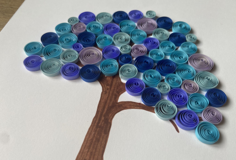 A picture of a brown tree trunk with spiraled paper leaves of various shades of blue.