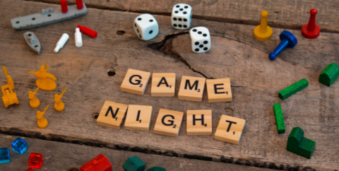 "Game Night" written with Scrabble letters, surrounded by other miscellaneous game pieces. 