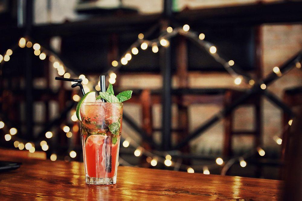 A pink mocktail with two straws sits on a wooden table.